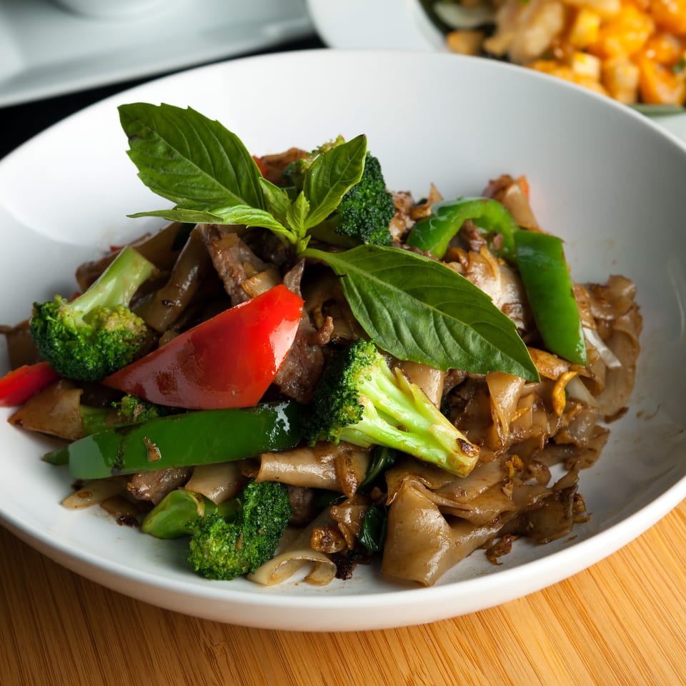 Chang Noi Thai's Pad See Ew with wide noodles, broccoli, bell peppers, and basil in a white bowl.