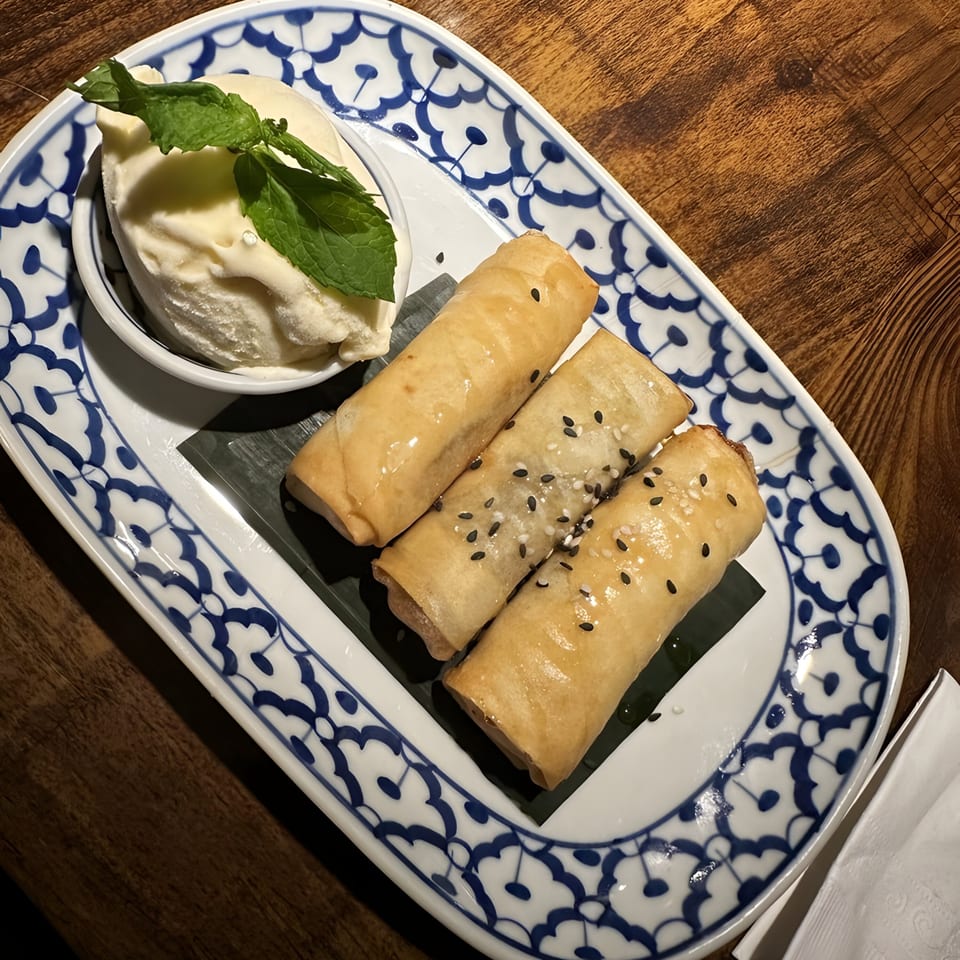 Three crispy Thai banana spring rolls with sesame seeds, served with vanilla ice cream and mint.